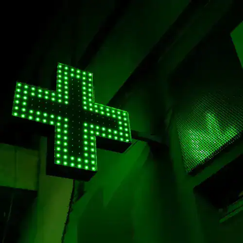 Green LED illuminated pharmacy cross sign on building exterior at night.