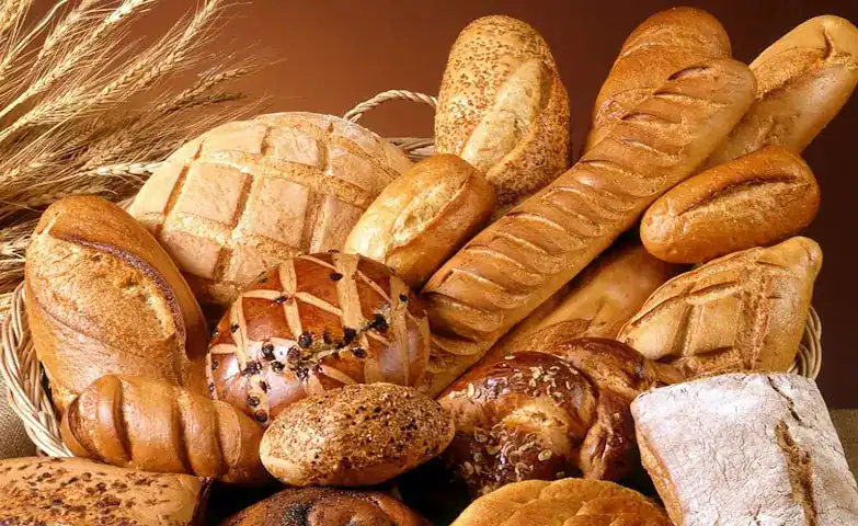 A variety of baked bread including baguettes, rolls, and loaves displayed in a basket.