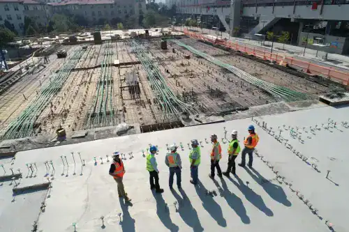 Construction workers inspecting a concrete slab at a building site in Beverly Hills, NSW, with ongoing rebar installation and safety gear.