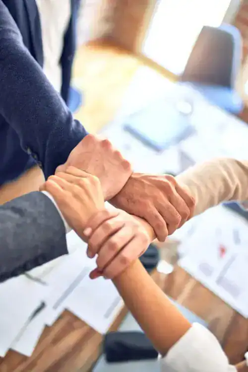 Team handshake, representing trust and teamwork in a business environment, with people in formal attire engaging in a handshake over a table with documents.