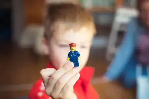 Young boy holding a small LEGO toy figure, focus on the toy with the boy's face blurred in the background.