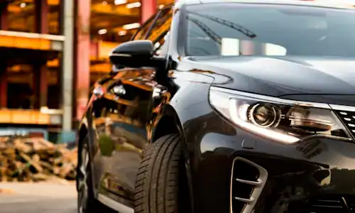 A sleek black sedan parked at a construction site with building materials and scaffolding in the background, showcasing modern automotive design and urban environment.