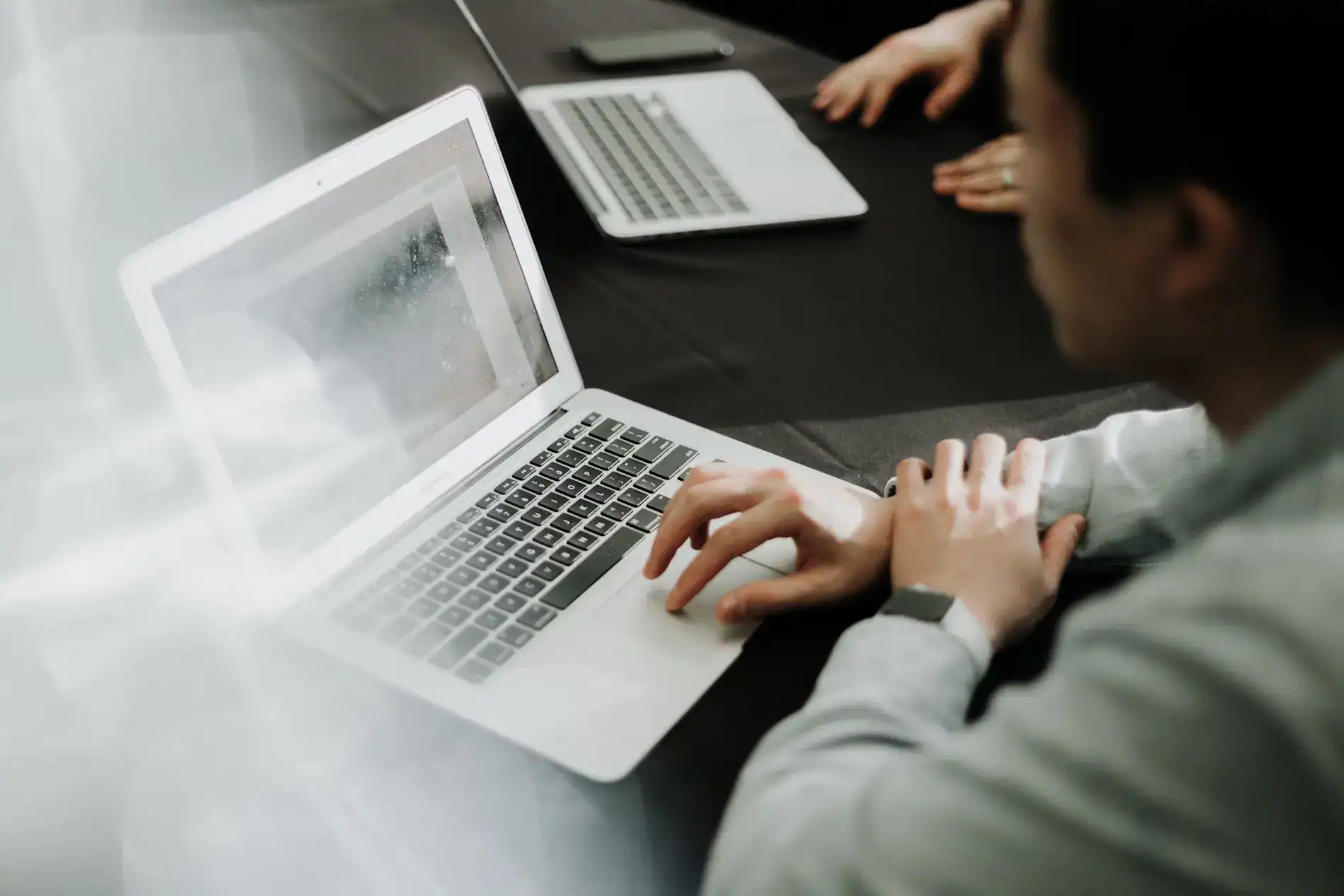 Two professionals collaborating over laptops during a business meeting, focusing on financial or accounting work in a modern office setting.