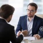 A professional tax advisor in a blue suit and glasses consulting with a client in an office setting, discussing financial matters.