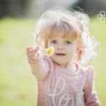 Child with curly blonde hair wearing a pink sweater, pointing towards the camera.