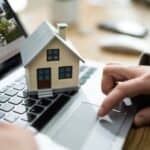Small model house placed on a laptop keyboard, symbolising real estate and property management online.