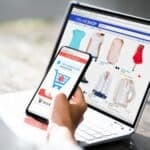 Person browsing fashion items on an online store via laptop and mobile device.