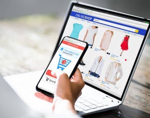 Person browsing fashion items on an online store via laptop and mobile device.