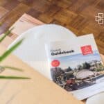 A guest guidebook for Airbnb guests placed on a wooden table, featuring a cover with a cityscape and the Airbnb logo, providing essential travel and accommodation details.