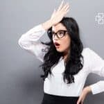 Top 10 Mistakes in Data Entry and Bookkeeping Woman with glasses looking surprised, hand on forehead, wearing white shirt against grey background.