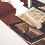 Person placing gingerbread cookies on an oven tray for baking, with a focus on holiday baking in a home kitchen.