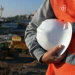 Construction worker in safety gear holding a white helmet at a construction site in Australia.