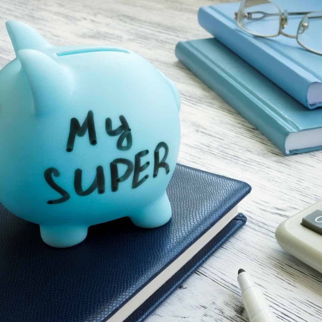 Blue piggy bank with "My Super" written on it, placed on a desk with notebooks, glasses, and a calculator, symbolising savings and financial planning.