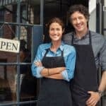 Business owners smiling outside their shop, showcasing friendly service and a positive customer experience.