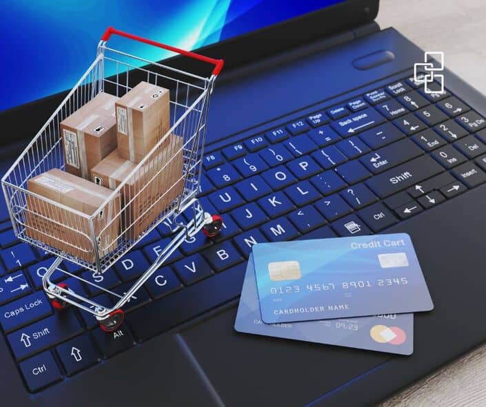 Small shopping cart filled with cardboard boxes placed on a laptop keyboard alongside a credit card, symbolising online shopping, e-commerce, or financial transactions.