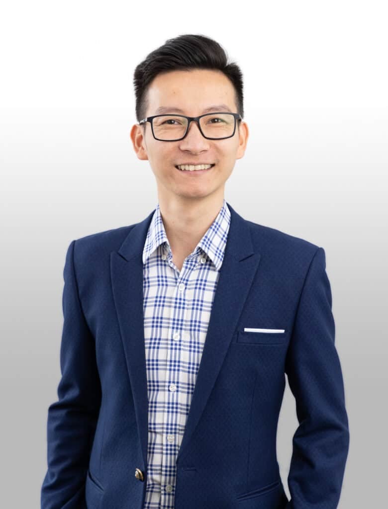 Smiling Australian accountant wearing glasses and a blue suit, standing confidently against a plain background.